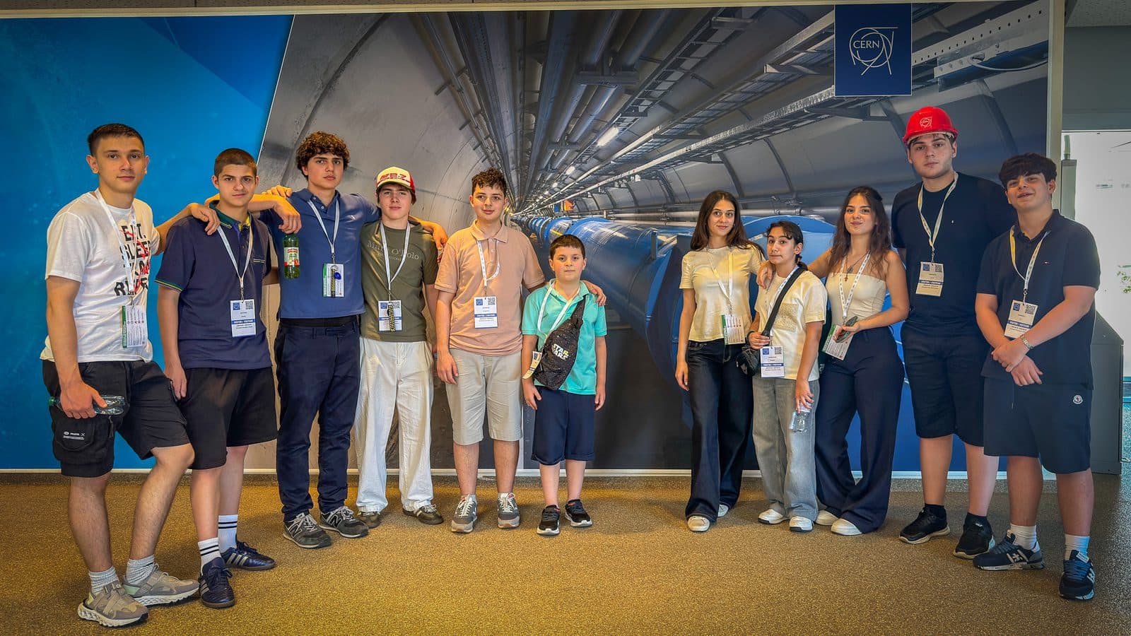 A Science Expedition group at CERN, in front of an image of the Large Hadron Collider tunnel