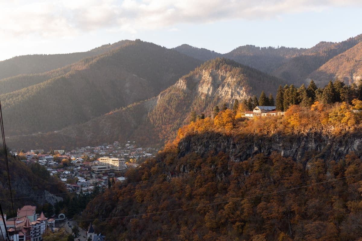 A wooded river gorge in southern Georgia in autumn: orange and green ridges above a town on the valley floor, with cable-car wires crossing the frame