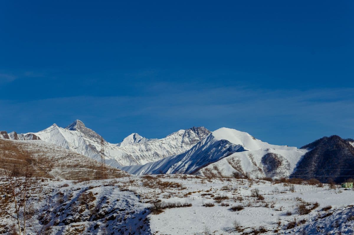 Snow-covered Caucasus peaks above the bare white slopes of the Gudauri plateau under a clear sky