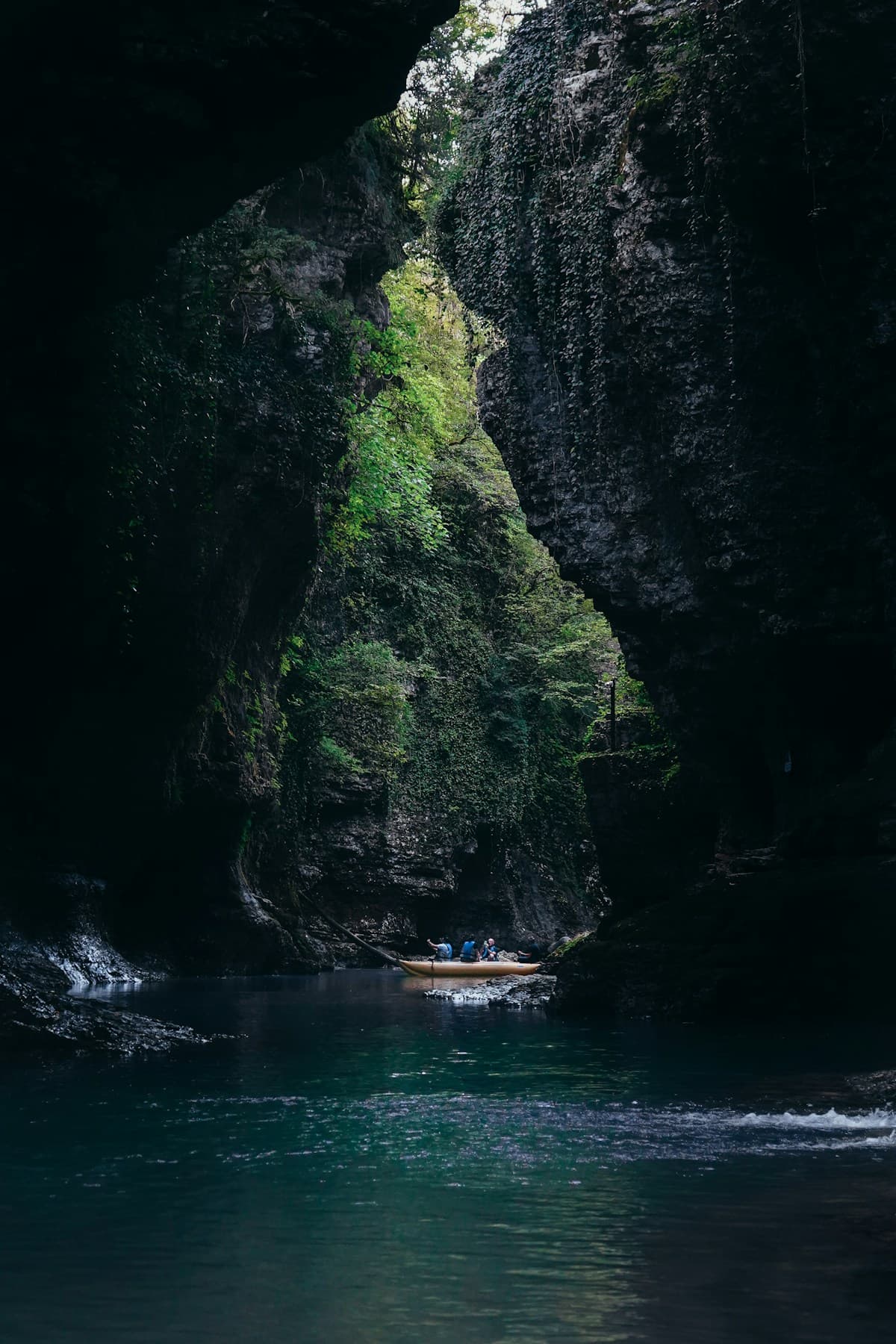 An inflatable boat carrying passengers in life jackets along green water walled in by cliffs