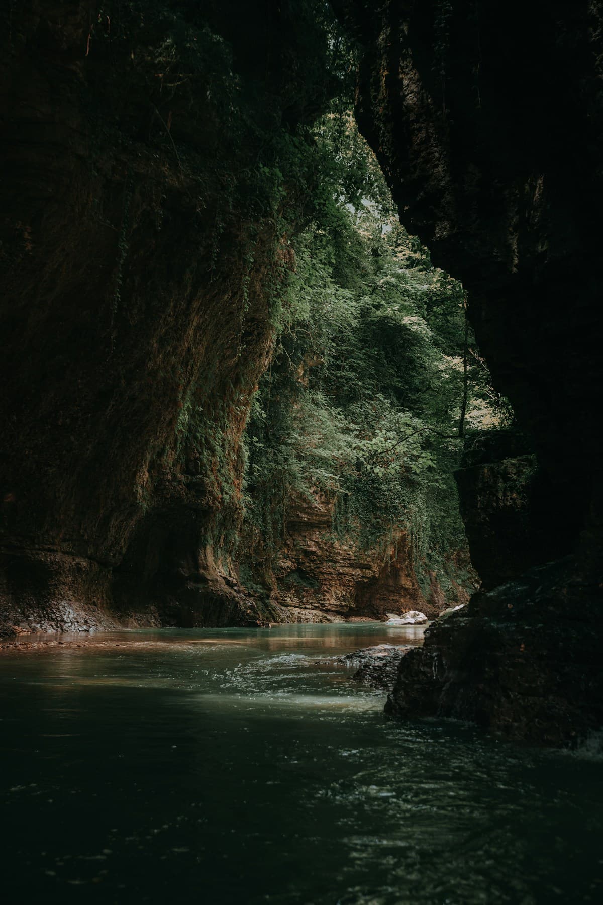 Turquoise water between mossy limestone walls in a narrow canyon, with a footbridge above